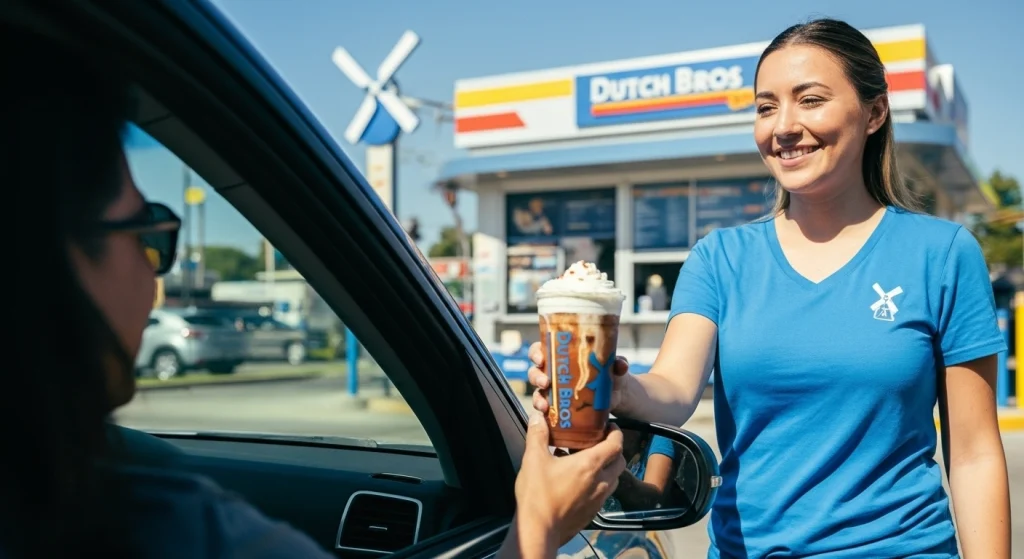 A blue shirt with smile woman giving a iced coffee drink to a car person.
